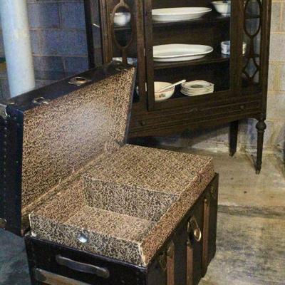Antique trunk, antique china cabinet with stoneware platters, china, and ceramic serving pieces.
