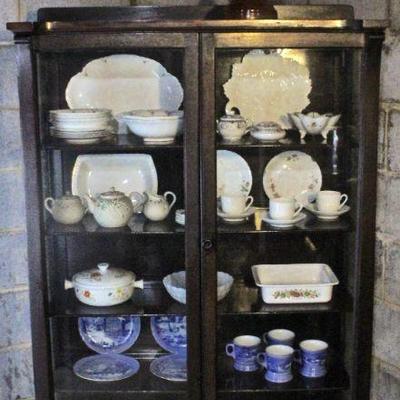 Antique china cabinet with ceramic serving pieces, mugs, cups & saucers, and bake ware.