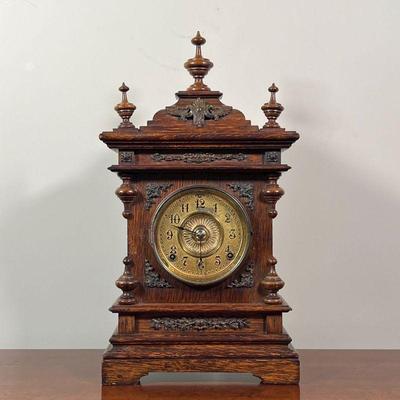ANSONIA SHELF CLOCK | Carved oak wood case with three finials and brass appliquÃ©, the face with Arabic numerals, the movement marked...