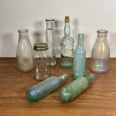 (8pc) GLASS BOTTLES  |  Including blue/purple iridescent glass bottles, an Evergreen Farm milk bottle, and others - h. 10.75 in. (tallest)