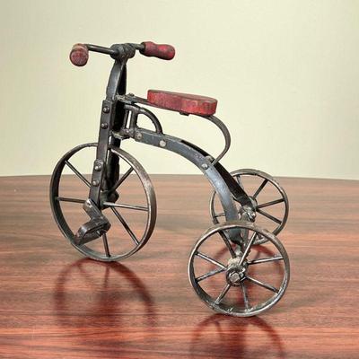 MINIATURE TRICYCLE  |
Small articulating metal tricycle having red wooden handle bars and a red wooden seat - h. 9 1/2 in.
