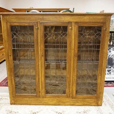 1010	LEADED GLASS TRIPLE DOOR BOOKCASE IN WOOD GRAINED FINISHED CASE, SOME LOSS TO GLASS, APPROXIMATELY 66 IN X 13 IN X 17 IN HIGH
