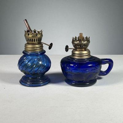 (2PC) PAIR HONG KONG BLUE GLASS OIL LAMPS | Made in Hong Kong, one lamp with fruit reliefs and handle in cobalt blue, the other with a...