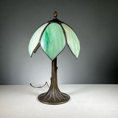 ART NOUVEAU SLAG GLASS LAMP | Table lamp with green petal-form slag glass shade on a tree trunk form bronzed metal base, with an acorn...