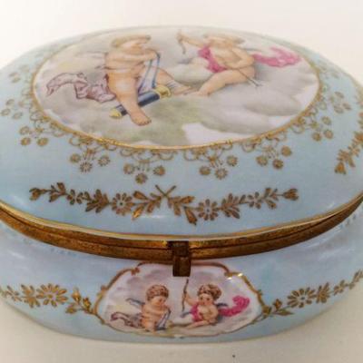 1127	PORCELAIN OVAL HINGED DRESSER BOX W/IMAGES OF CHERUBS & ROSE INTERIOR, APPROXIMATELY 5 IN X 7 IN X 4 IN HIGH
