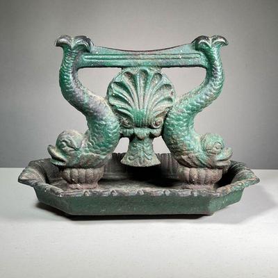 ANTIQUE CAST IRON BOOT SCRAPER | Decorated with dolphins (fish) and a central seashell and with old green paint. - l. 14 x w. 10 x h. 10 in