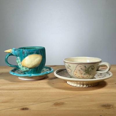 (2PC) ART POTTERY CUP & SAUCERS | Two sets, including a figural bird cup signed Bernadette, and a Strawberry Design cup signed Anna...