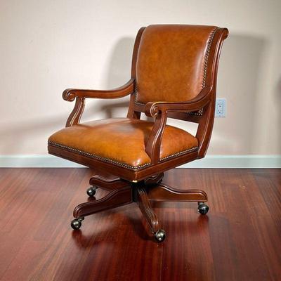 LEATHER EXECUTIVE DESK CHAIR | Rolling office chair with carved wood armrests and rivets bordering the brown leather back and seat...