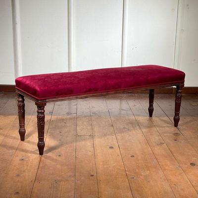 Carved Upholstered Bench | Having an overall red upholstered cushion over a wood sub-structure resting on turned straight legs, decorated...