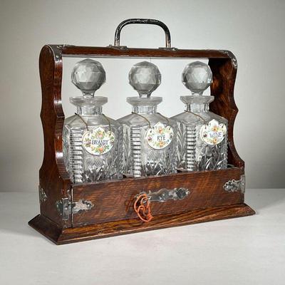 Cased Decanters Set | Three crystal decanters each with porcelain labels (brandy, rye, wine) nested in a wood carrying case with lock and...