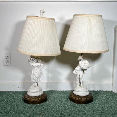 (2PC) PAIR BISQUE FIGURINE LAMPS | Pair of white bisque figurine lamps depicting a man and a woman in elegant clothing atop brass base. -...