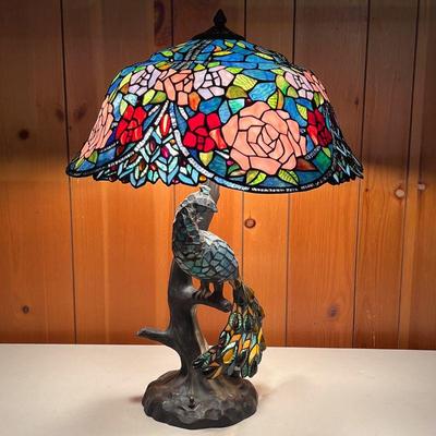 PEACOCK STAINED GLASS LAMP | Peacock sitting on a branch of the tree-shaped base. Shade has large pink roses. There is a small bulb...