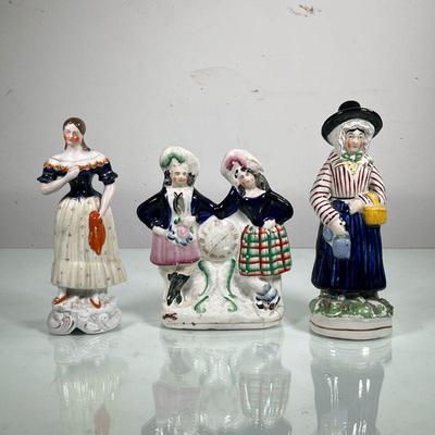 (3PC) FEMALE CERAMIC FIGURINES | Includes pair of women leaning on clock, dressed up women with picnic basket and woman in fancy dress. -...