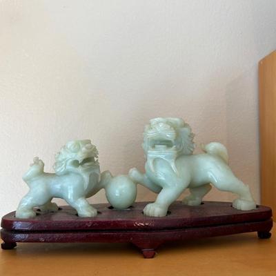 CHINESE CARVED HARD PALE GREEN TONE STONE BUDDHIST LIONS WITH A BALL, ON A WOODEN STAND