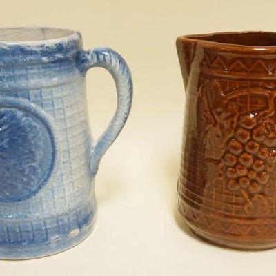 1214	2 STONEWARE PITCHERS, ONE W/EMBOSSED AMERICAN INDIAN & OTHER EMBOSSED W/GRAPES & VINE, APPROXIMATELY 8 1/4 IN HIGH

