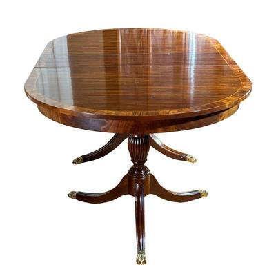 HENKEL-HARRIS CO. MAHOGANY DINING TABLE | Oval mahogany dining table over double carved pedestal with brass pedestal feet. Includes 4...