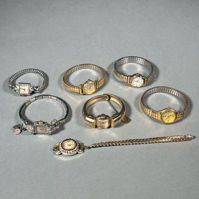 (7PC) LADYâ€™S WRISTWATCHES | Base metal watches in gold and silver tones, including a Alsta watch with sterling silver religious charms.
