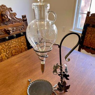 Lot 054-K: Suspended Wine Decanter

Description: 
â€¢	Wine decanter with decorative metal vines along the stand and etched grapes on the...