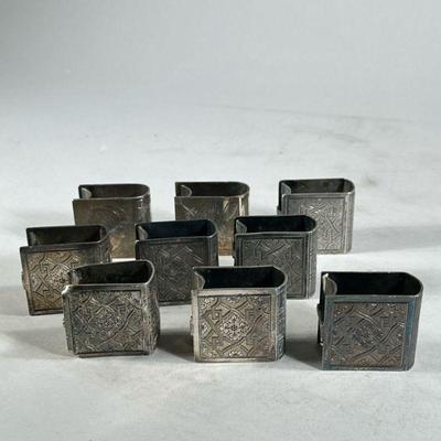 (9PC) SILVER PLATE NAPKIN RINGS | Silver plate napkin rings in the shape of books decorated with floral and geometric patterns with space...