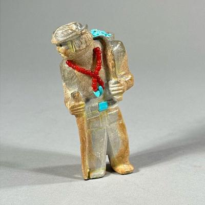 FREDDIE LEEKYA ZUNI FETISH CARVING | Showing figure of a man with beadwork necklace carrying collection of turquoise. Signed “FL” on...