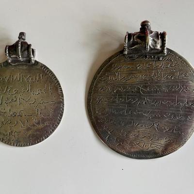 A pair of Omani silver Samt pendants with text from the Quran on the front and a shackled jinn on the reverseâ€”these were worn to ward...