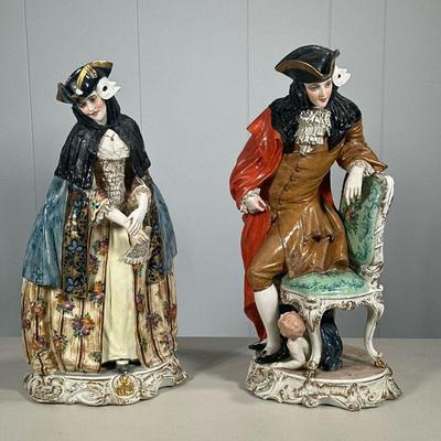 (2PC) PAIR LARGE MASQUERADE FIGURINES | Showing man and woman in masquerade ball attire with child hiding under man’s chair, painted with...