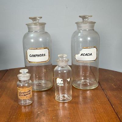 (4PC) BLOWN GLASS APOTHECARY JARS | Including two large jars, one Camphora another Acacia, plus two smaller jars. - h. 11.5 in (tallest)

