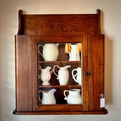 Antique wall cabinet with collection of white/ivory pitchers