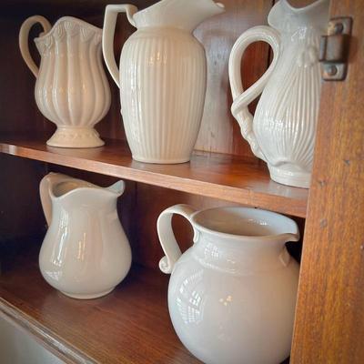 Antique wall cabinet with collection of white/ivory pitchers