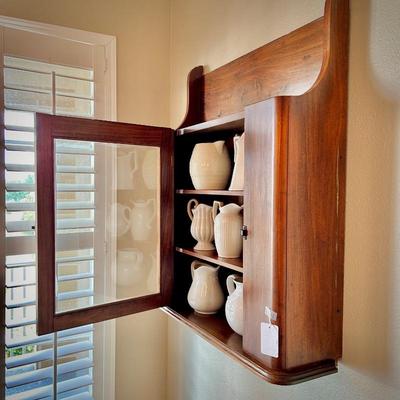 Antique wall cabinet with collection of white/ivory pitchers