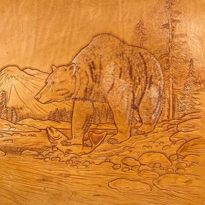 LEWIS J. BRICE LEATHER ART | Burnished / embossed leather art of a bear catching salmon from a river before a mountainous landscape, with...