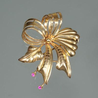 18K GOLD RIBBON FORM PIN | Designed as an 18 karat gold pierced open work, ribbon form pin with a leaf and mounting two rubies; 2 in.,...