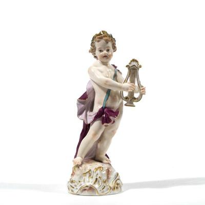 MEISSEN PORCELAIN FIGURE | A porcelain figure of cupid with lyre or other musical instrument in a purple / red cape, with underglaze blue...
