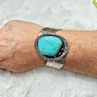Sterling Silver cuff bracelet features a large, oval turquoise stone set in a detailed silver band with hand carved embellishments.