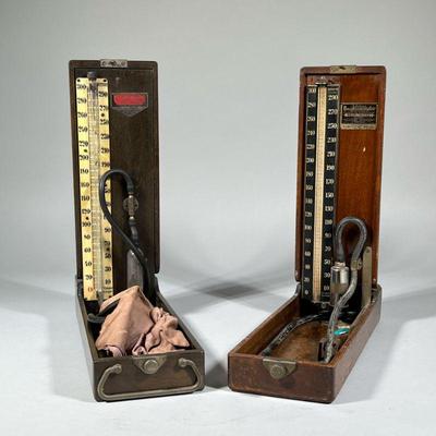 (2pc) EARLY BAUMANOMETERS BLOOD PRESSURE MEDICAL DEVICES | Two "Baumanometer" tabletop blood pressure checkers in fitted wood...