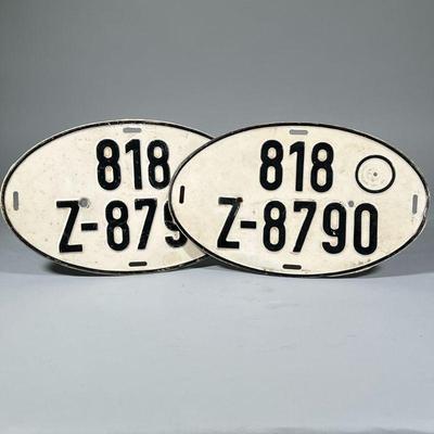 (2pc) VINTAGE LICENSE PLATES | Two vintage German license plates of oval shape with black pressed lettering on a white enamel ground. -...