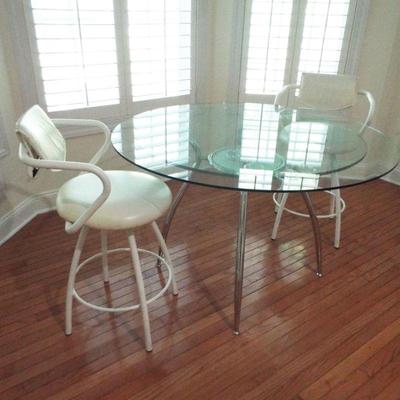 STAINLESS EATING UTENSILS UNDER GLASS TOP ROUND TABLE
WHITE VINYL STOOL TYPE CHAIRS

