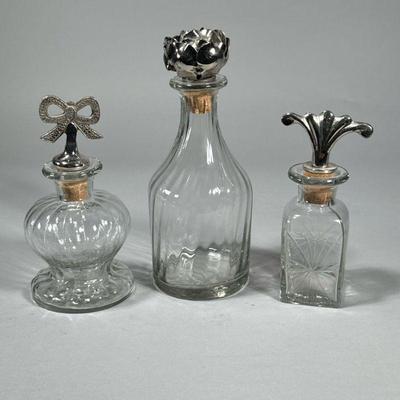 (3pc) GLASS BOTTLES WITH PEWTER STOPPERS | Decorative glass bottles with figural pewter stops. - h. 9 in (tallest)

