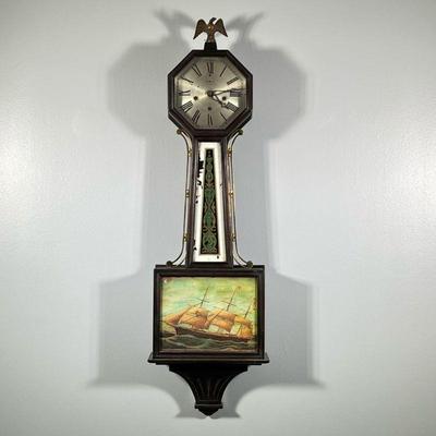 NEW HAVEN CLOCK CO. BANJO CLOCK | Crested by an eagle finial, octagonal face, brushed metal with Roman numerals, eglomise central panel...