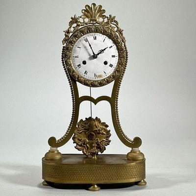 BRASS SHELF CLOCK | Gilt brass frame with acanthus scroll and shell crest, rose pattern surrounding the white face with Roman numeral...
