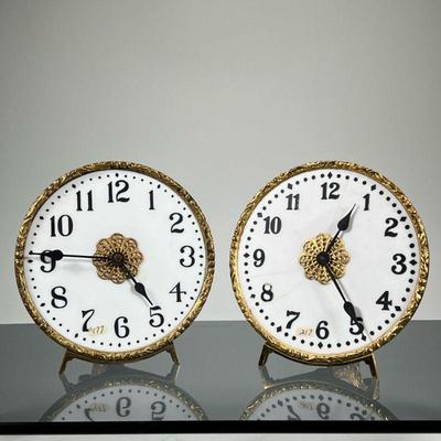 (2pc) PAIR PORCELAIN & BRASS EASEL CLOCKS | Each having a gilt frame with folding easel back, the faces with black Arabic numeral...