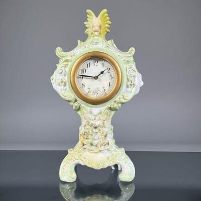 AMERICAN PORCELAIN CLOCK | Sculpted porcelain with floral decoration and gilt highlights, crested by a figural head at the top, the face...