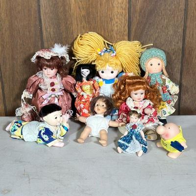 (9pc) Small Porcelain & Other Dolls | Including a reach for the stars applause doll, a fabric doll in a 2002 Beijing dress, and other...