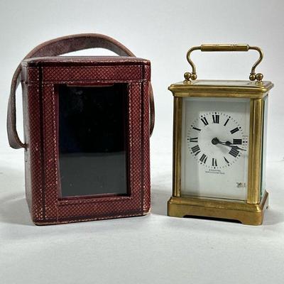 EMANUEL SOUTHAMPTON CARRIAGE CLOCK | A brass carriage clock with five beveled glass panels in a red leather carrying case, the face with...