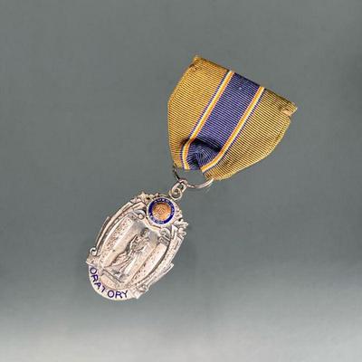 STERLING AMERICAN LEGION BADGE | Sterling silver American Legion Oratory medal with blue enamel, on a striped ribbon fastened pin;...