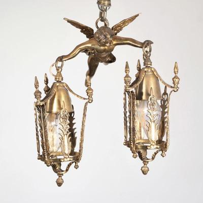 CUPID BRASS FIGURAL TWO-LITE HANGING FIXTURE | Gilt toned metal brass hanging light fixture designed as Cupid suspending two lanterns...