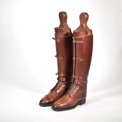 "BROWN RIDING BOOTS & FORMS | A pair of brown leather riding boots with lace holes and straps and with a pair of a wooden boot...