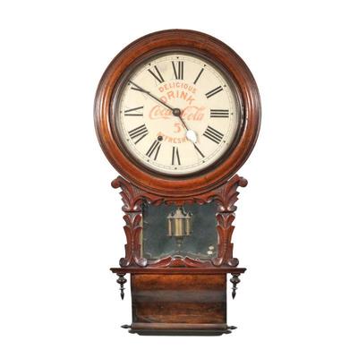 "COCA-COLA WALL CLOCK | In a carved wood case with mirror behind pendulum, the face with Roman numeral markers and reading,...