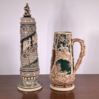 (2pc) Large German Steins | German steins both numbered. One has lid and writing and the other depicts a hunting scene, each with...