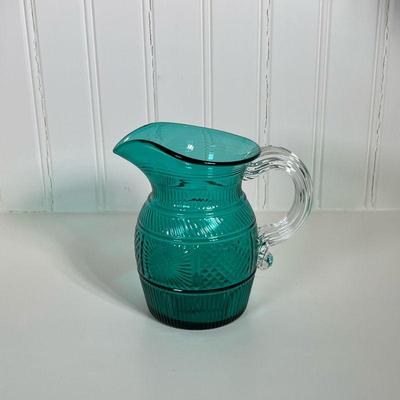 Small Green Glass Pitcher | Glass green textured patterned pitcher marked "MMA" with clear glass handle. Dimensions: h. 6.5 x...